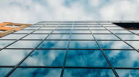 Zeigt die Glasfront eines Gebäudes welche eine Wolkendecke spiegelt